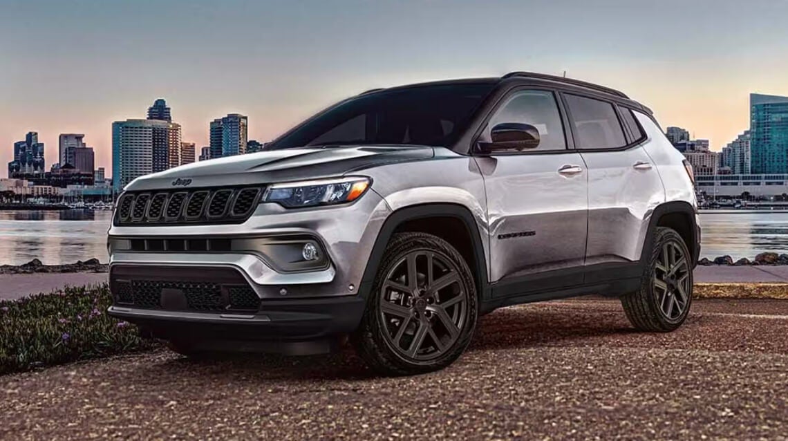 A Silver Jeep Compass parked in a waterfront lot with a city skyline in the background.
